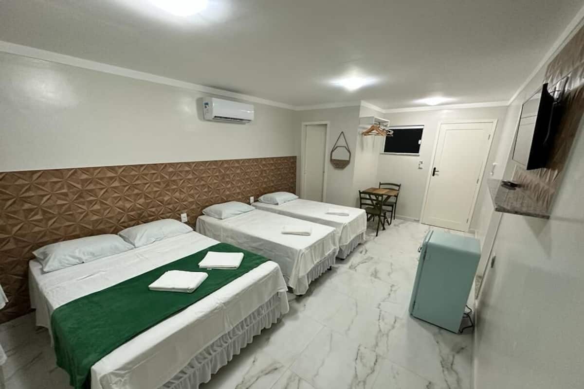 A hotel room with two beds, a small table, a chair, a TV, and a refrigerator.