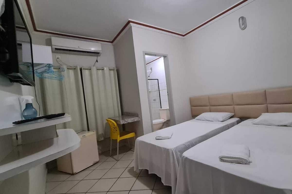 A hotel room with two beds, a desk, a chair, a window, and a bathroom.