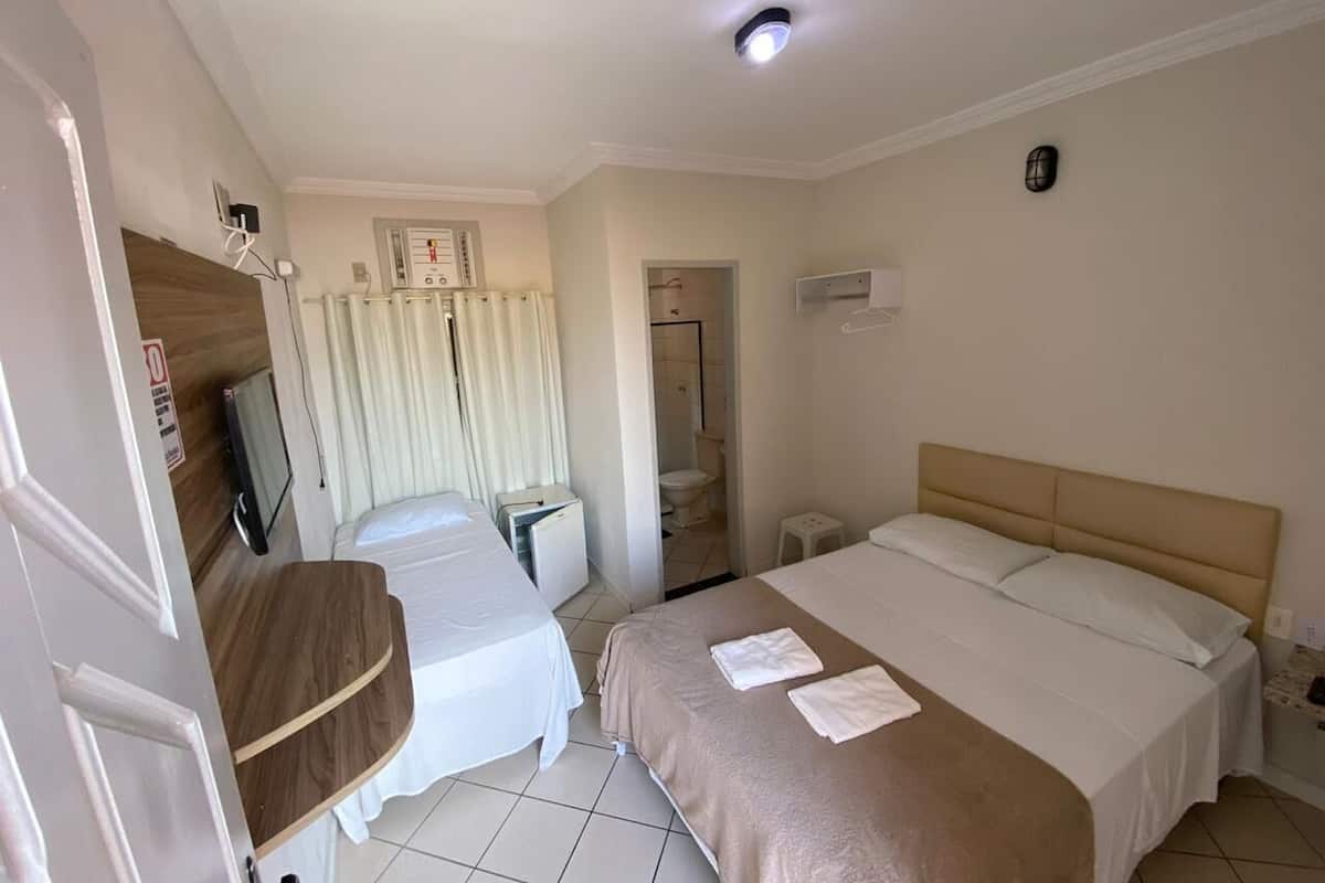 A hotel room with two beds, a small desk, a mirror, and a shower area.