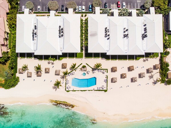 Vista aérea de um resort com vários edifícios de telhado branco, uma piscina central e acesso à praia.