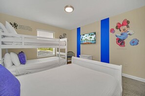 Habitació d'hotel amb llits superposats, un llit gran, una finestra amb persianes, una paret amb un mural de Minnie Mouse i una taula petita.