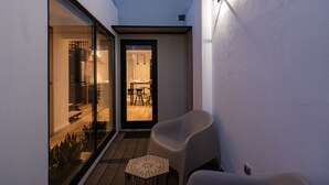 Un patio exterior moderno con una puerta de vidrio que da a un área de comedor, una silla blanca y una pequeña mesa.