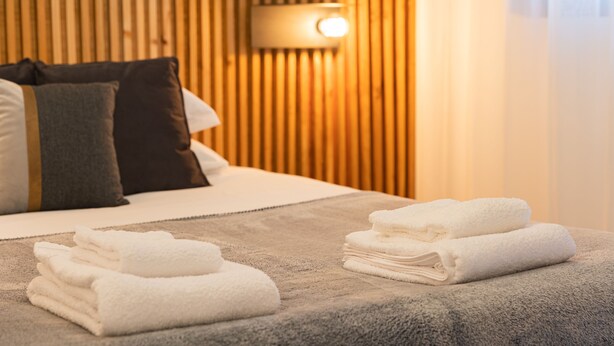 Una cama bien hecha con toallas blancas, un cabecero de madera y una lámpara fijada a la pared.