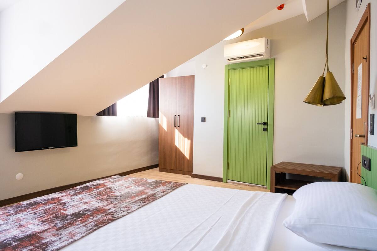 A bedroom with a bed, a green door, a television, and a small wooden table.
