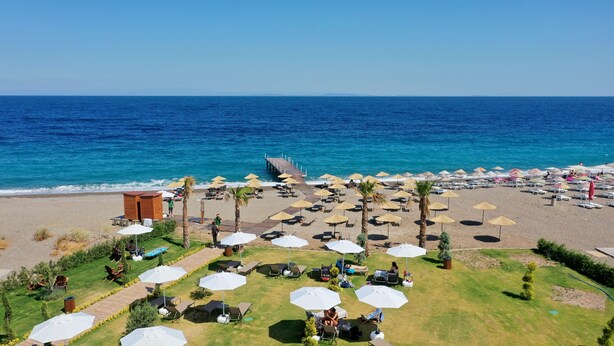 Um resort à beira-mar com espreguiçadeiras, guarda-sóis e um píer que se estende para o mar.