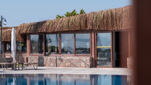 Uma área de piscina com um edifício de telhado de palha, espreguiçadeiras e vista clara da piscina.