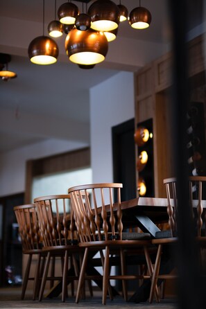 A dining area with multiple wooden chairs and a table, under a series of hanging pendant lights. - ASSOS TROY BEACH HOTEL (Ayvacik)