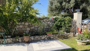 A stone wall with potted plants, a tiled patio, and a grassy area with stepping stones. - Flat - Sleeps 2 - Parking - Patio (Kefalonia)
