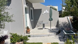 A modern outdoor patio area with a round table and chairs, a small seating area with a table and chairs, and a staircase leading to an upper level. - Flat - Sleeps 2 - Parking - Patio (Kefalonia)