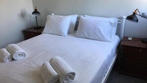 A neatly made bed with white linens and rolled towels, a bedside lamp, and a small wooden nightstand. - Flat - Sleeps 2 - Parking - Patio (Kefalonia)