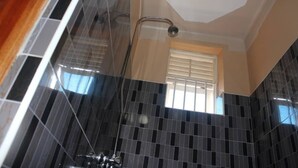 A bathroom with dark tiled walls, a shower, and a window with blinds. - Atotti Prime City Hotel (Soroti)
