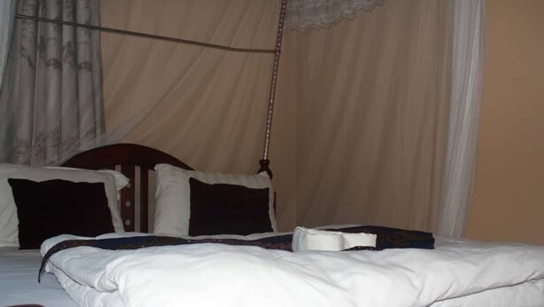 A bed with white bedding, a wooden headboard, and a hanging mosquito net. - Atotti Prime City Hotel (Soroti)