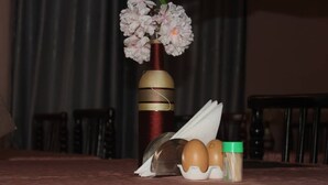 A table with a vase of flowers, a thermos, a napkin, and a container with eggs and a spice jar. - Atotti Prime City Hotel (Soroti)