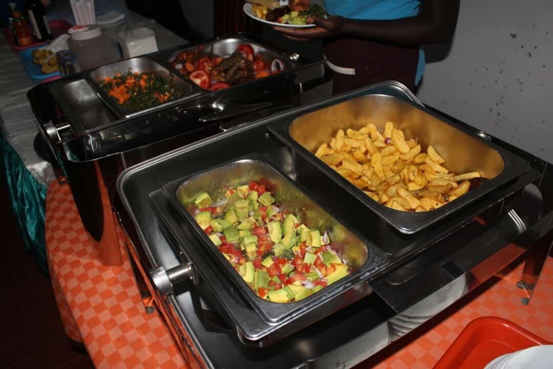 A buffet with various food options including a tray of avocado and tomato salad, a container of French fries, and other dishes.