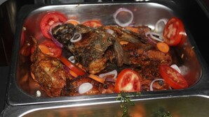 A fish dish with tomatoes and onions in a stainless steel sink. - Atotti Prime City Hotel (Soroti)