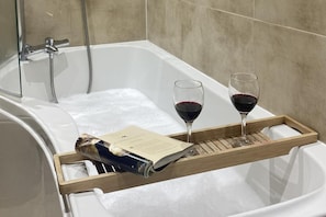 A bathtub with two glasses of red wine and a book on a tray.