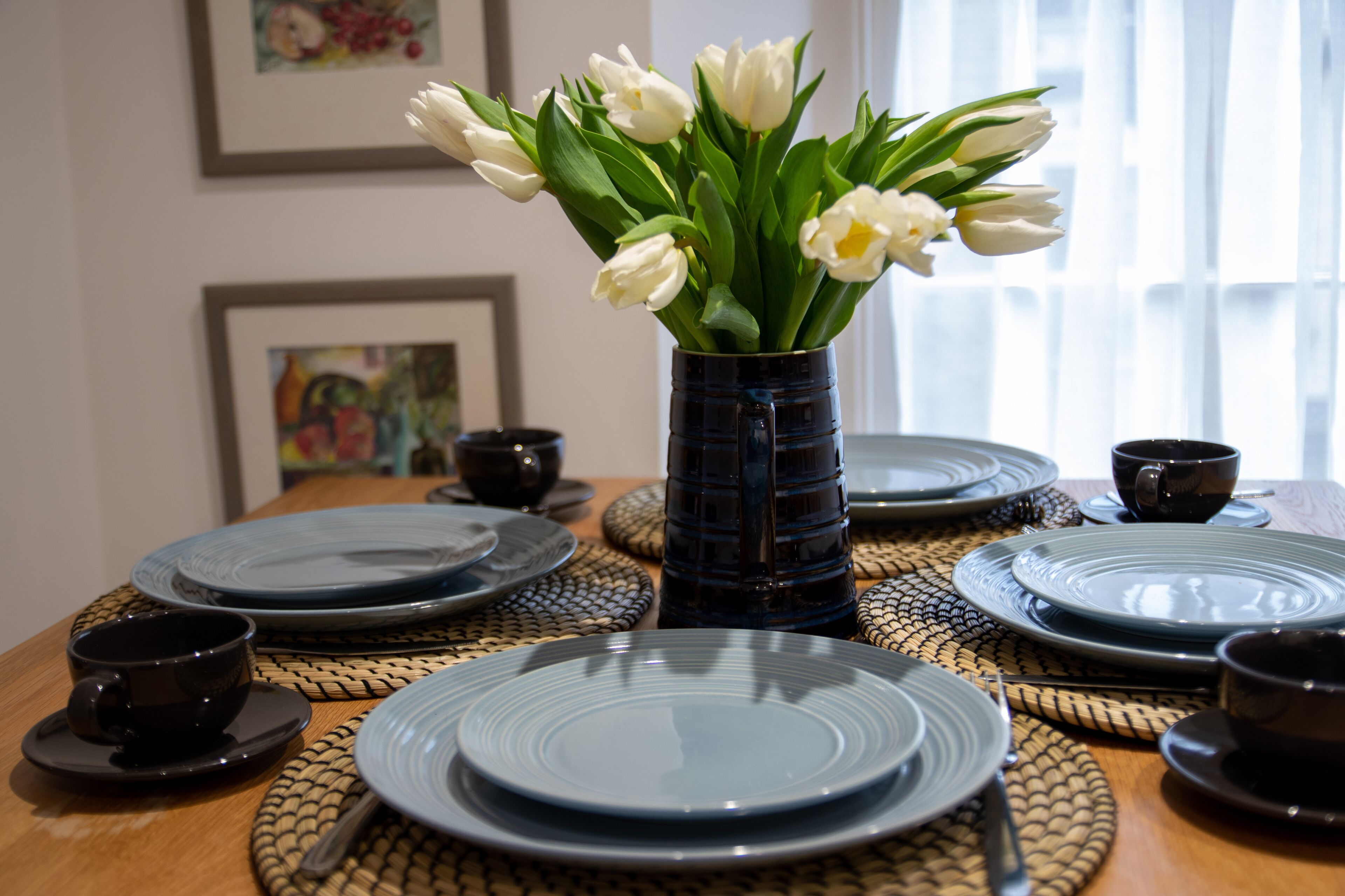 Een eettafel gedekt met borden, kommen en een vaas witte tulpen.