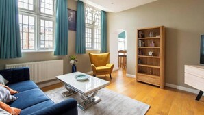 A living room with a blue sofa, a yellow armchair, a wooden bookshelf, and a white coffee table. - The Best Apartment in Canterbury (Canterbury)