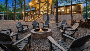 Een lodge met een stenen gevel, een houten terras en een vuurkuil omringd door Adirondack-stoelen.