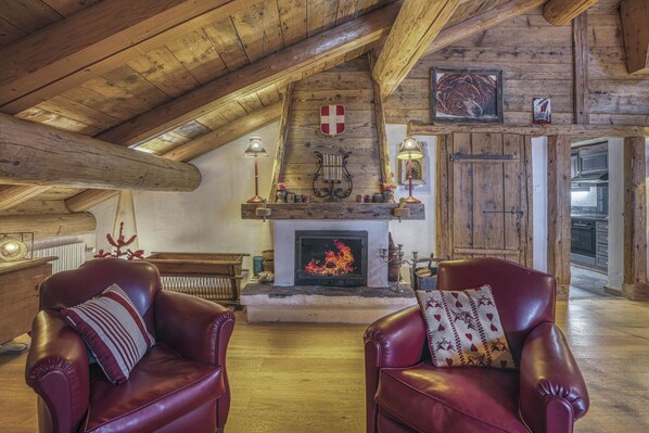 A cozy room with a fireplace, leather chairs, wooden beams, and a shield emblem on the wall. - La Grange Paccaly, 4* Appartment, Heart Village (La Clusaz)