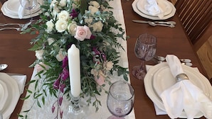 Een gedekte eettafel voor een formeel diner, met witte borden, bestek en glazen, omringd door houten stoelen.
