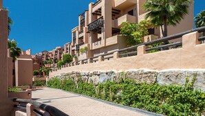 A modern hotel with multiple balconies, a stone retaining wall, and lush greenery. - Coto Real 2311 Sea View (Manilva)