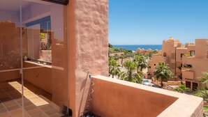 A balcony with a view of a coastal town, a clear sky, and a sandy wall. - Coto Real 2311 Sea View (Manilva)