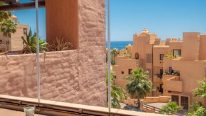 A view from a window overlooking a coastal area with traditional architecture and palm trees. - Coto Real 2311 Sea View (Manilva)