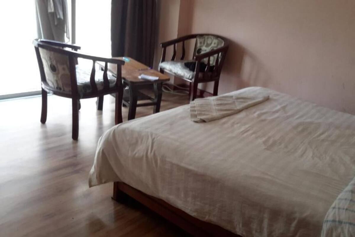 Ein Hotelzimmer mit Bett, zwei Stühlen, einem kleinen Tisch und einem Fenster mit Vorhängen.