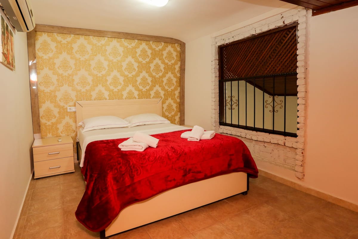 Una cama bien hecha con una colcha y almohadas rojas, un cabecero de madera y una mesita de noche con cajones.