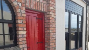 Une porte rouge avec une poignée noire, un mur de briques et une fenêtre à cadre noir.