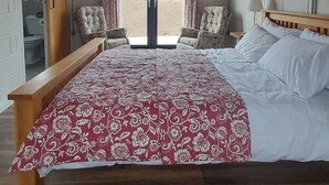 Une chambre avec un grand lit, un plancher en bois, un ventilateur de plafond et une vue sur l’extérieur grâce à une porte coulissante.