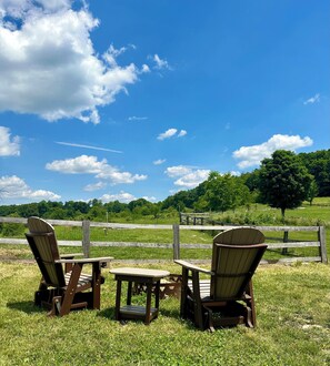 Two Adirondack chairs, a wooden table, and a wooden fence in a grassy field with a clear blue sky. - StarGazer 2.0 FARM cottage, just 20 mins to hocking hills. w/fast internet (McArthur)