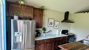 Une cuisine moderne avec des meubles en bois, un réfrigérateur en acier inoxydable, un îlot central en bois avec un tabouret de bar et une machine à café.