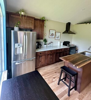 Una cocina moderna con armarios de madera, un refrigerador de acero inoxidable, una isla de madera con un taburete y una cafetera.