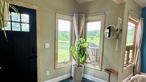 Une pièce avec un parquet en chevrons, une grande plante en pot, un miroir et un luminaire au plafond.