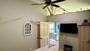 Une chambre avec un lit, un ventilateur de plafond, une télévision et une armoire.