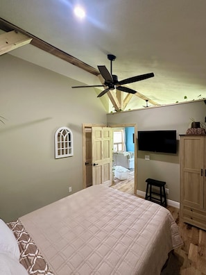 Une chambre avec un lit, un ventilateur de plafond, une télévision et une armoire.