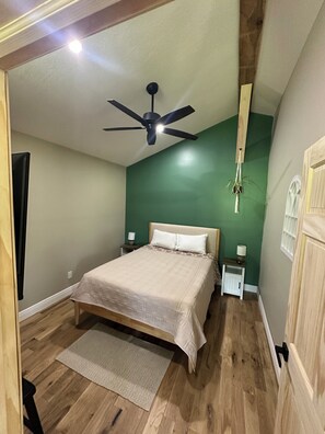 A bedroom with a bed, a ceiling fan, a nightstand, a lamp, and a wooden floor. - StarGazer 2.0 FARM cottage, just 20 mins to hocking hills. w/fast internet (McArthur)