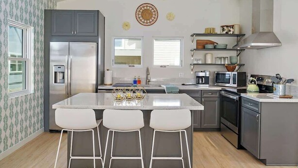 Una cucina moderna con isola centrale, sgabelli da bar, elettrodomestici in acciaio inossidabile e decorazioni a parete.