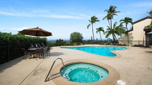 Un espace piscine comprenant un jacuzzi, des chaises longues et une table avec un parasol.