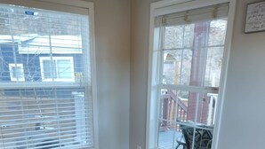 Quarto com piso de madeira, duas janelas com persianas e vista para um deck com móveis de exterior.