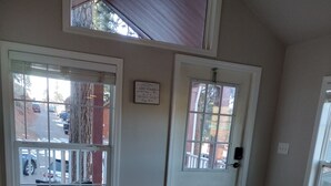 Um quarto com piso de madeira, um sofá bege com almofadas estampadas e uma porta branca com janela.