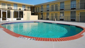 A swimming pool with a red brick border, surrounded by a building with balconies and a yellow facade.
