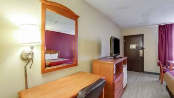 A hotel room with a wooden desk, a chair, a television, a dresser, a mirror, and a door.