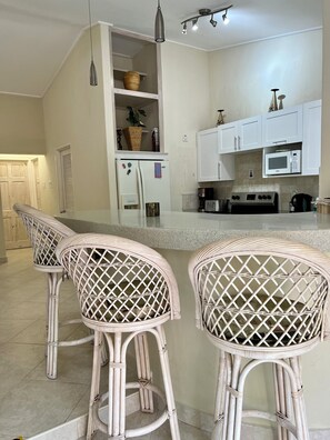 A kitchen with white cabinets, a microwave, a stove, and wicker bar stools.