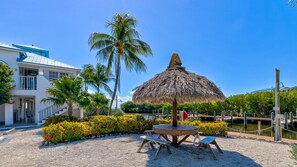 A beachfront property with a thatched umbrella, a wooden table, and benches.