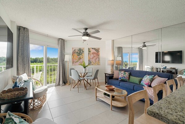 A spacious living room with a blue sofa, a dining table, and a balcony with a view.