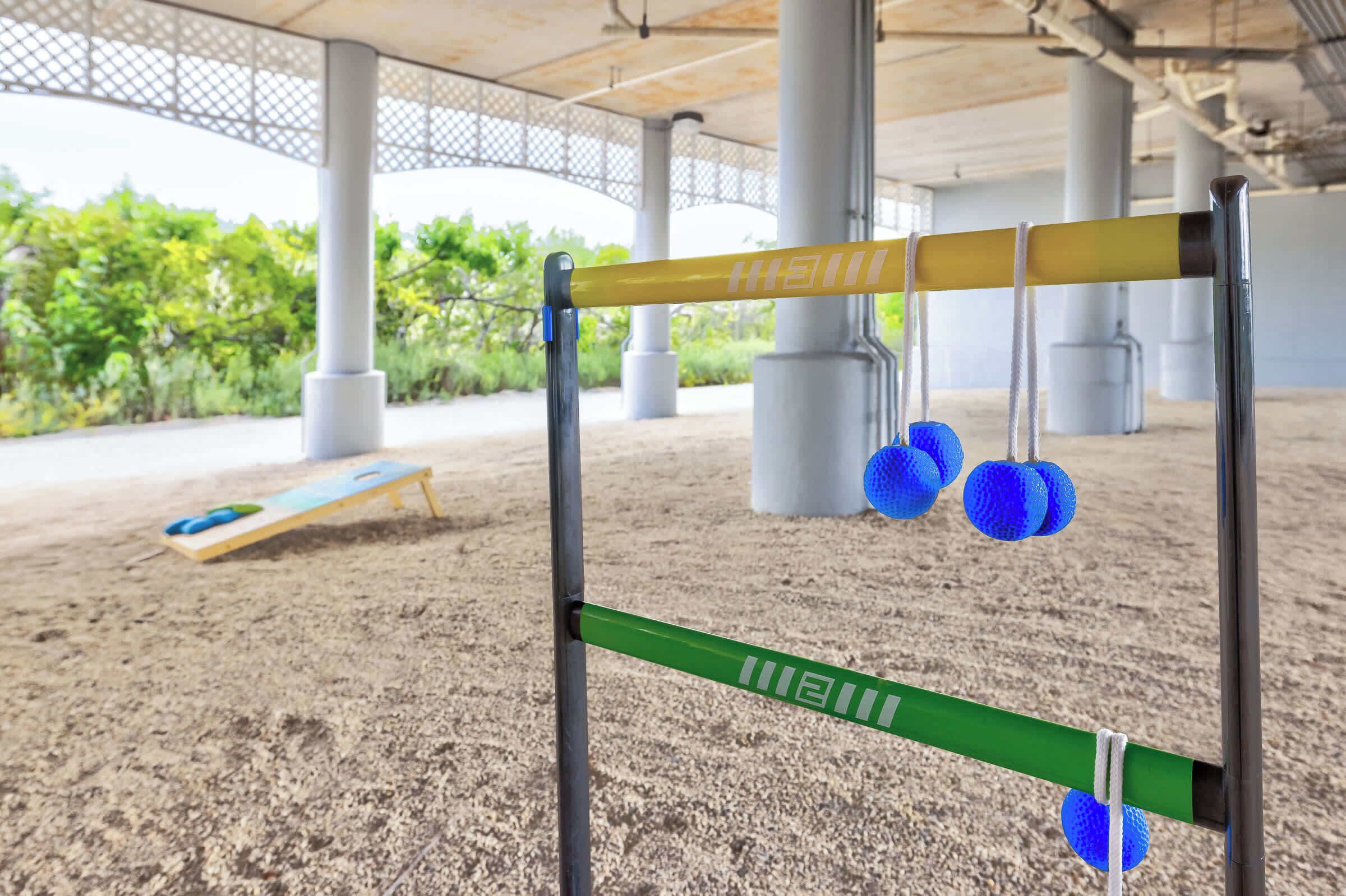 Zona arenosa al aire libre con equipo de ejercicio, incluyendo una viga de equilibrio y pelotas azules.