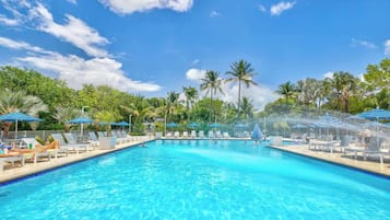 A swimming pool with lounge chairs and umbrellas, surrounded by palm trees.